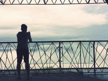 Rear view of woman standing by railing against sky