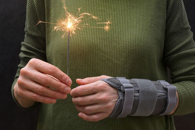 Midsection of woman holding illuminated sparkler with bandage on hand
