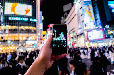 Cropped hand of man photographing city through smart phone at night