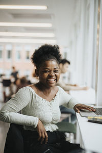 Portrait of cheerful student with laptop sitting at table in university