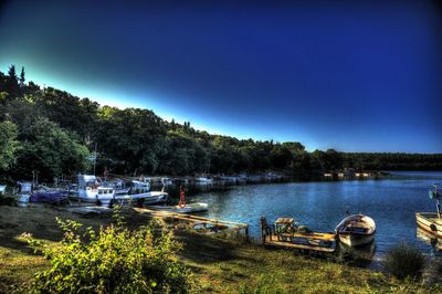 Boats moored at harbor against clear blue sky