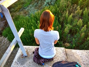 Rear view of woman sitting on rock against trees