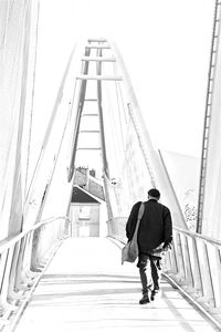 Rear view of man walking on bridge against clear sky