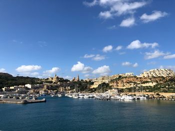 Sailboats in sea by city against sky