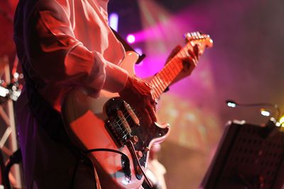 Midsection of man playing guitar in music concert