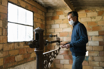 Worker wearing protective mask weighing grapes on old-fashioned scale at winery