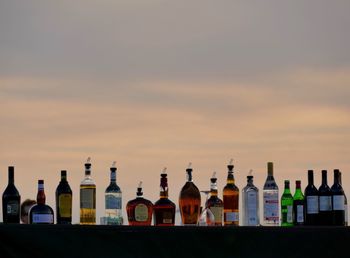 Alcohol bottles arranged on retaining wall against sky during sunset