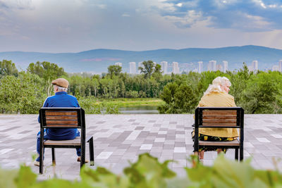 Rear view of man sitting on bench against plants