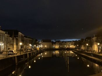 Canal by illuminated city against sky at night