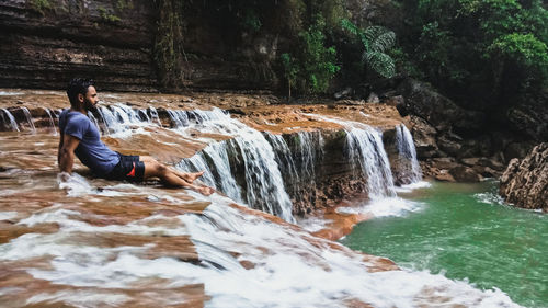 Man sitting on waterfall at forest