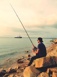 Man fishing while sitting on rock at beach