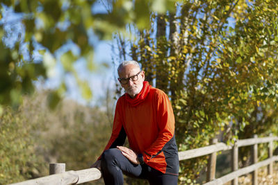 Portrait of senior man leaning on fence in park