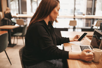 Adult confident serious smiling business woman freelancer working in cafe using a laptop and phone