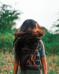 Woman flipping hairs while standing against trees