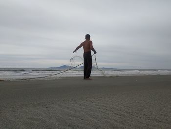 Rear view of man standing on beach against sky
