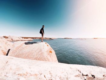 Man on rock by sea against clear sky