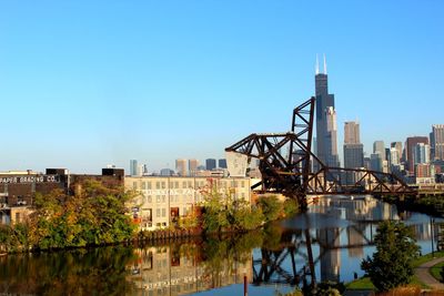 Buildings by river against clear blue sky