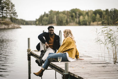 Smiling male and female partners sitting on pier over lake during social gathering