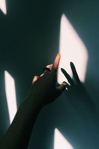 Cropped hand of woman by shadows on white wall