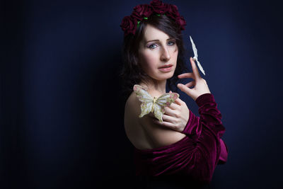 Portrait of young woman holding rose against black background