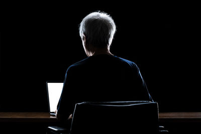 Rear view of man sitting on table against black background