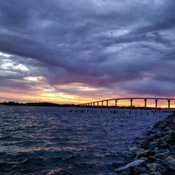 Silhouette of bridge over sea against cloudy sky