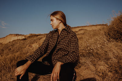 Young woman sitting on land against sky