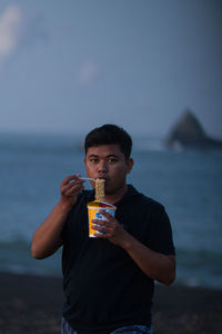 Portrait of young man standing in sea against sky