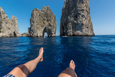 Low section of people on rock by sea against sky