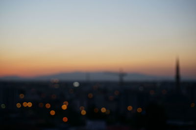 Defocused image of illuminated city against clear sky at sunset