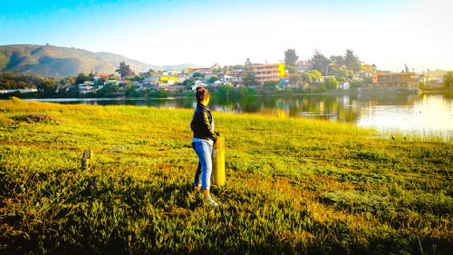 Side view of woman standing on grassy lakeshore during sunset