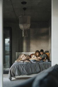 Happy lesbian couple sharing smart phone while sitting on bed in bedroom
