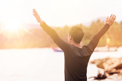 Rear view of man with arms raised standing at beach on sunny day