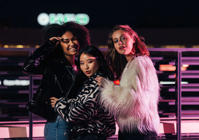 Portrait of smiling women standing by railing outdoors at night