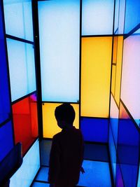 Rear view of silhouette boy standing by colorful wall