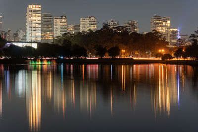 Illuminated buildings by lake against sky in city at night