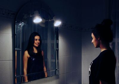 Young woman standing against illuminated wall at night