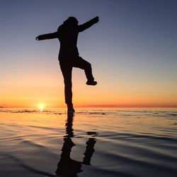 Silhouette man standing on beach at sunset