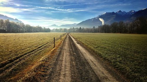 Dirt road by landscape against sky