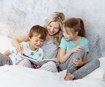 Mother and children reading book on bed at home