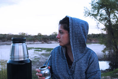 Woman drinking mate at sunset near the river. 