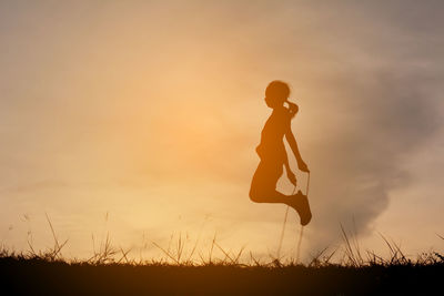 Silhouette girl skipping on field against sky during sunset