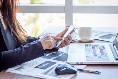 Midsection of businesswoman using phone at desk in office