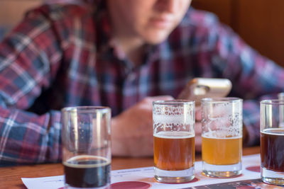 Midsection of man using phone while having beer at table