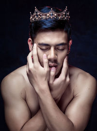 Close-up of young man wearing crown against black background