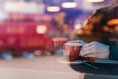 View through window of woman hands holding cup of coffee