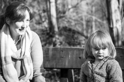 Woman with her daughter looking away while sitting on bench