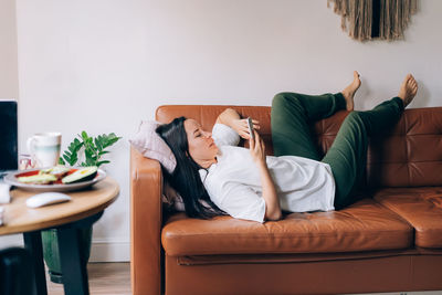 Attractive latin woman lies relaxed on the sofa in the living room in a comfortable position.