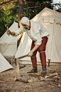 Man cutting wood on land by tents