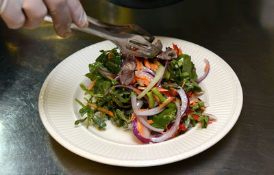 Close-up of hand serving salad with tongs in plate on table